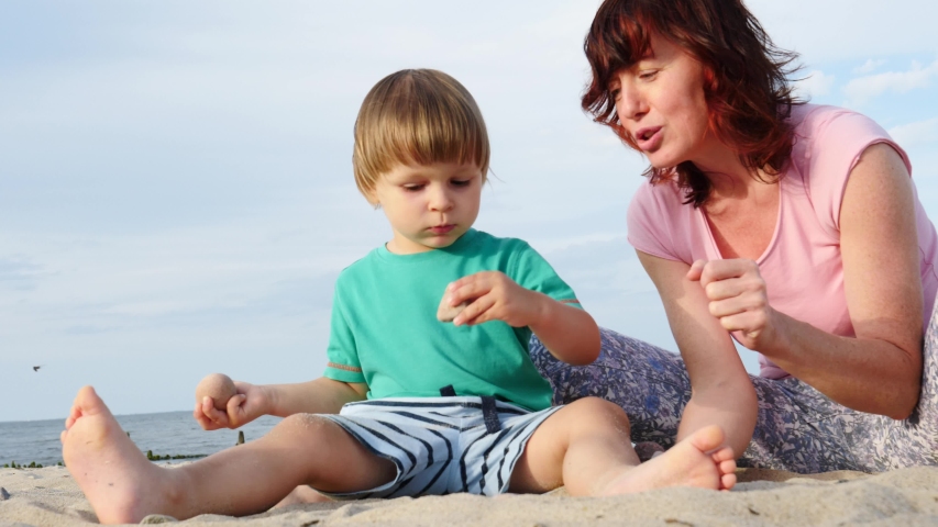 Mother playing with little child boy on sand beach. Adult woman and her son enjoying summer day on seshore. Family holiday at sea. Slow motion