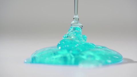 DETAILED: Turquoise gel pouring on white table and slowly lay down on the flatness. Light white studio room. 4-x slow motion, 100 fps to 25 fps video.