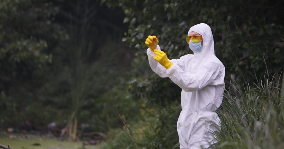 A scientist in a white protective suit holds a test tube in his hands and examines its contents.