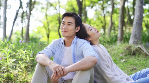 young asian couple sitting on ground outdoors in woods