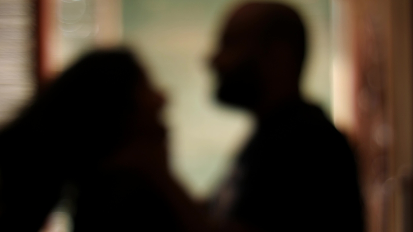 Medium closeup silhouetted and blurred view of a man choking a woman. Domestic violence. Husband beating his wife.