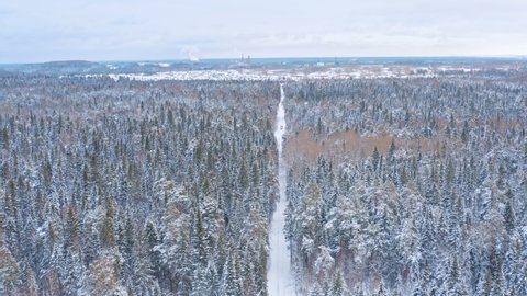 Drone view of red truck with cargo on snow covered empty road among winter snowy forest near an industrial town