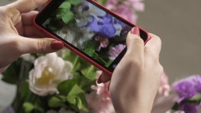 young florist girl at work shooting beautiful bouquet of roses and carnations on phone. Record videos for social networks. Flower business. Concept of A small floral shop. Creating a bouquet for sale.