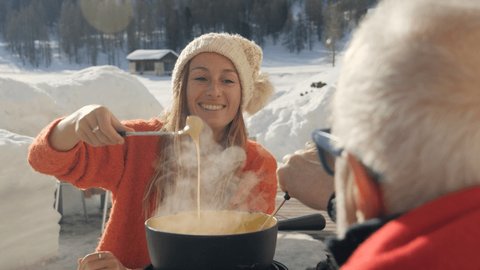 Mature man and young woman sharing cheese fondue in the Swiss Alps in winter, family enjoying meal together, snowcapped mountains ski holidays. Two people eating outdoor 