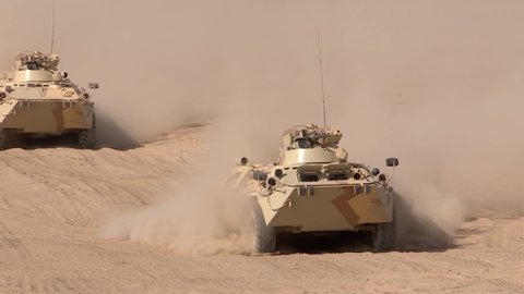 A military column of armored vehicles moves through the desert, raising dust. Special operation of the military.
