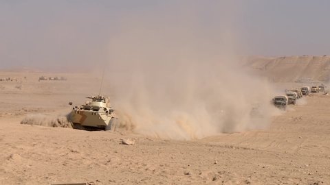 A military column of armored vehicles moves through the desert, raising dust. Special operation of the military 1