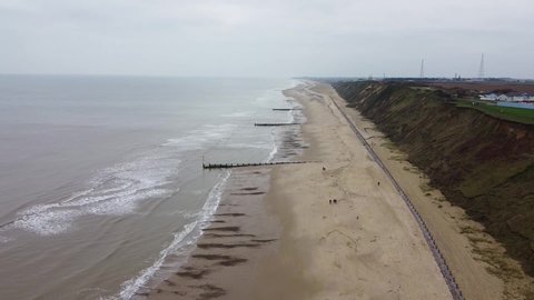 Aerial shot of the norfolk coastline in england, waves crashing into a beach divided by groynes
