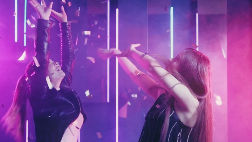 Neon women. Girls party. Joyful besties dancing in shiny confetti purple illumination.