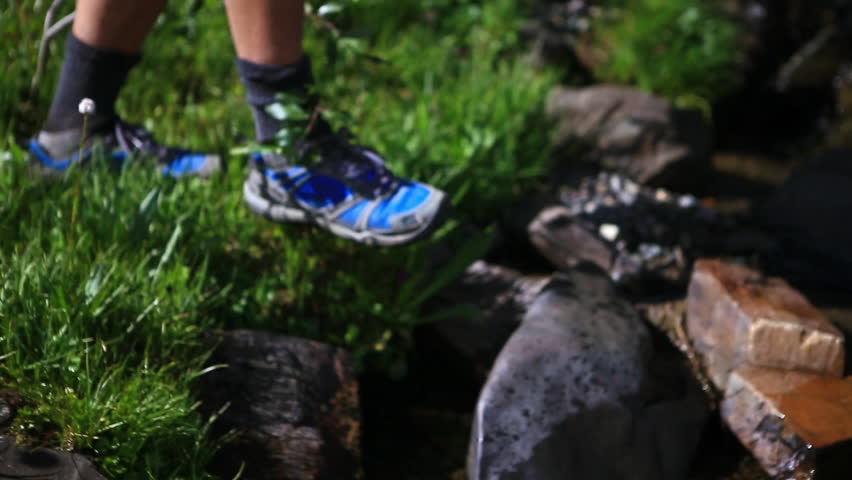 Hiker stepping on stones across stream