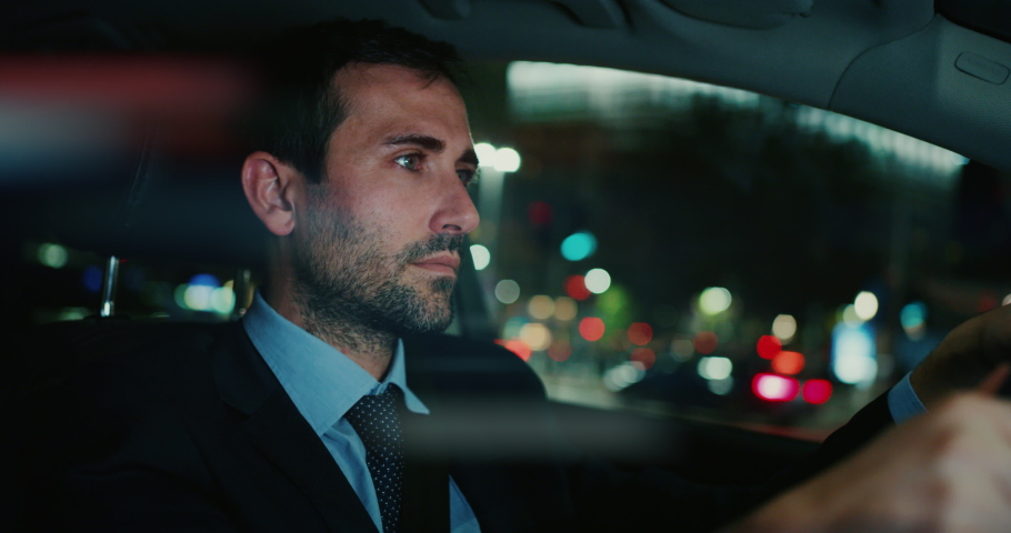 Slow motion of young handsome businessman driving a modern car in center of the city by night. Shot in 8K. Concept of business, success, traveling, luxury Royalty-Free Stock Footage #1045808839