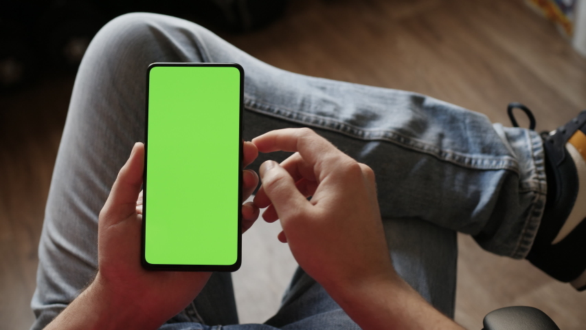 Man Using Smartphone in Horizontal Mode with Green Mock-up Screen, Doing Swiping, Scrolling Gestures. Guy Mobile Phone, Internet Social Networks Browsing News, Financial Reports. Point of View Camera