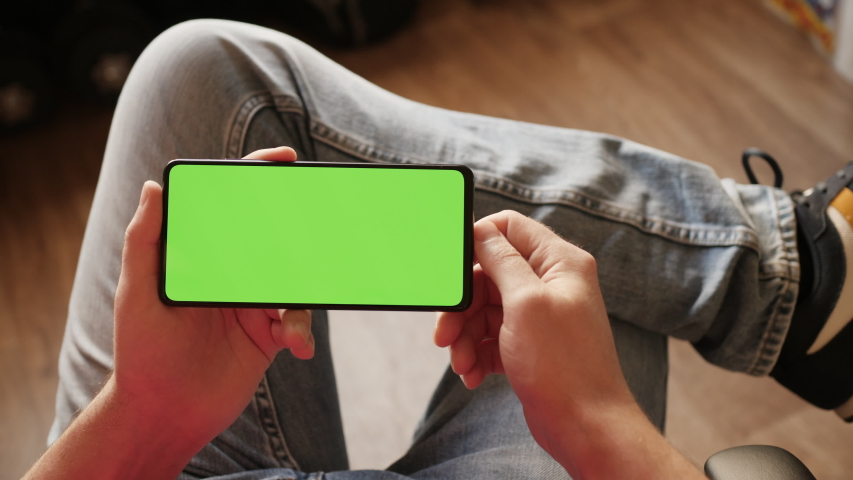 Man Using Smartphone in Horizontal Mode with Green Mock-up Screen, Doing Swiping, Scrolling Gestures. Guy Mobile Phone, Internet Social Networks Browsing News, Financial Reports. Point of View Camera Royalty-Free Stock Footage #1045816369