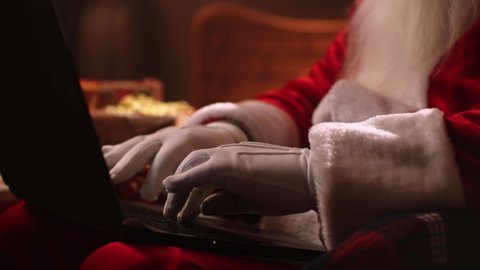 Santa Claus is working with a laptop looking through mail and answering messages to children. Choosing and ordering online gifts for children for Christmas.