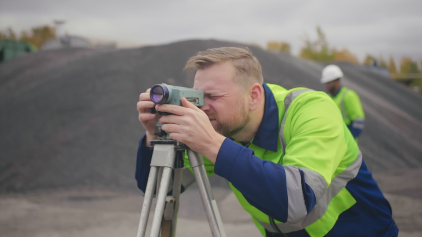 Constructor foreman with theodolite transit equipment at construction site outdoors during surveying work. Caucasian industrial worker using surveyor transit for measurement. Field works Royalty-Free Stock Footage #1045825936