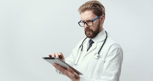 Portrait of confident medical specialist holding digital tablet over white background. Bearded doctor in white lab coat and black tie using modern technologies at work