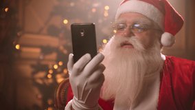 Santa Claus uses a smartphone and talks via video link while conducting a conference. Santa Claus and selfie camera, online broadcasts.