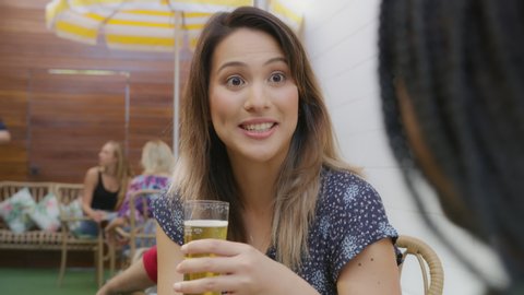 Young attractive woman sitting at restaurant talking having a beer on a patio with other patrons in the background. Medium close on 4k RED camera.