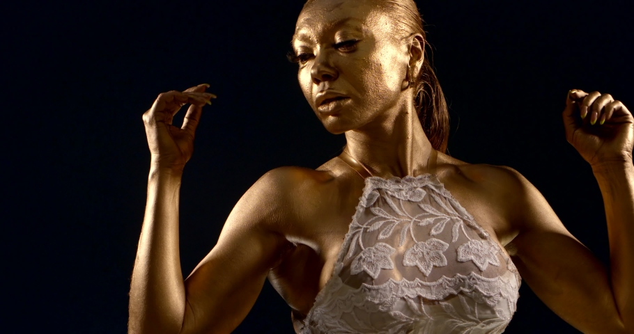 portrait of a woman with Golden skin and raised muscles in a lace top on a black background. she raises her hands, touches her hair, and turns sideways