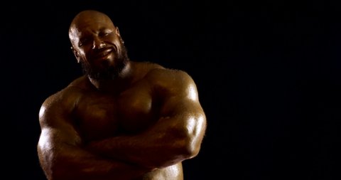 a bearded bald brutal male bodybuilder with a naked inflated torso, he is in the Studio on a black background, Posing, showing off his muscles and biceps. He crosses his arms over his chest.