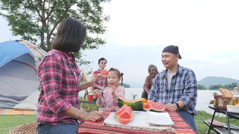 Little asian girl helping her mother to give watermelon slide to her grandparent.Happy time of asian family in camping site.