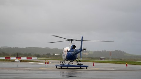 Stavanger / Norway - 11 03 2019: Helicopter sitting at heliport in the rain, rotor spinning while another helicopter flies overhead