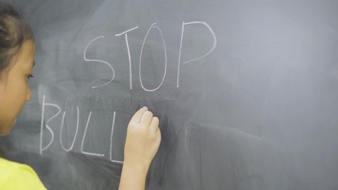 Female elementary school student writing a text of stop bullying on a blackboard in the classroom. Shot in 4k resolution