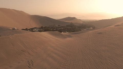 Sandy desert oasis lake. DRONE. Water in middle of hot sand desert. Romantic, holiday, honeymoon, scenic shot, with sand ripples and footprints. Tourism shot in Huacachina, Peru. Epic, dramatic shot. 