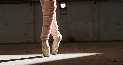 Close up of legs of a female ballet dancer practicing in an empty warehouse, standing on tiptoes and jumping, slow motion