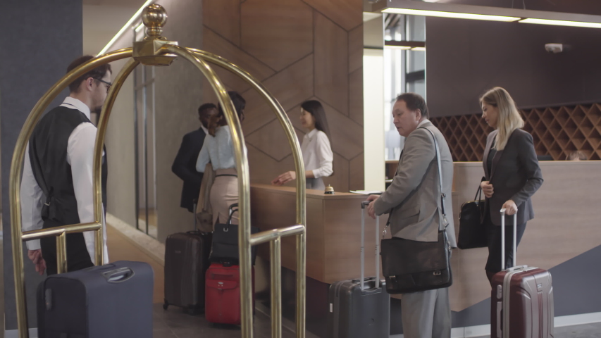 Tracking shot of professional bellman in uniform helping guests and putting their suitcases on luggage cart Royalty-Free Stock Footage #1045887967