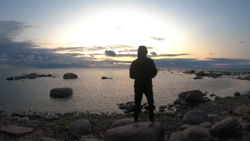 
young man stands on the background of the bay during sunset