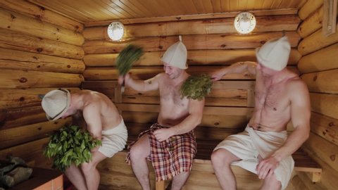 Athletic men in a sauna with brooms.