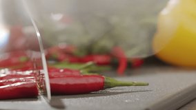 Cook cuts red chili peppers on kitchen board with sharp steel knife. Slow motion video