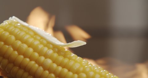 Piece of butter melts on hot corn with blazing fire in the background. Tasty young sweet corn. Slow motion video