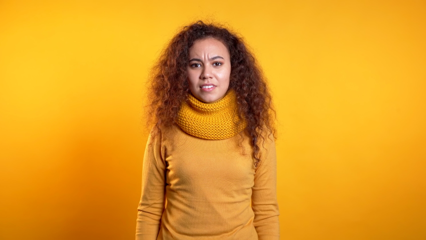 Young scared curly girl shouting isolated over yellow background. Stressed and depressed woman