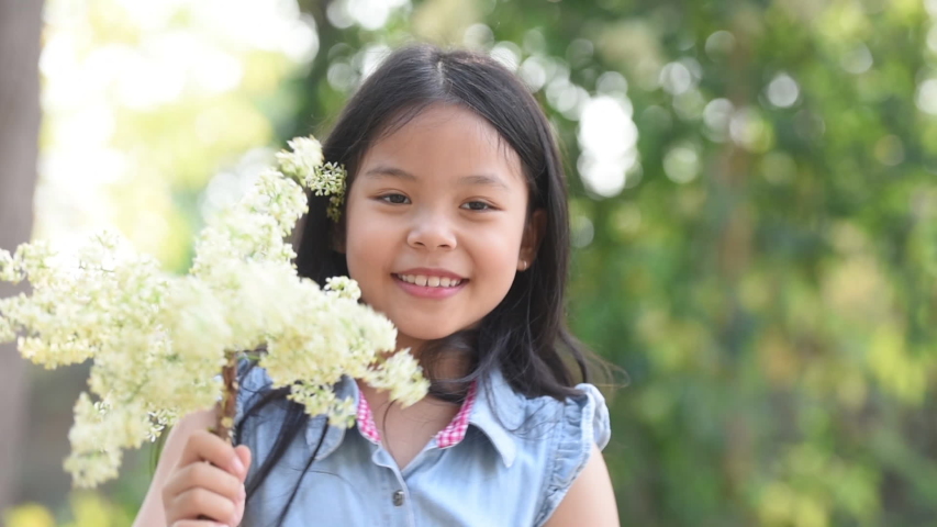 asia girl playing in flower field. Kid in the backyard. nature and fun. child holds a bouquet of wildflowers in his hands. Selective focus. Happy little asian girl in the field. environment, ecology.