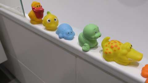 Rubber squishy toy collection in a row on bathtub ledge. Medium shot. High angle view. 