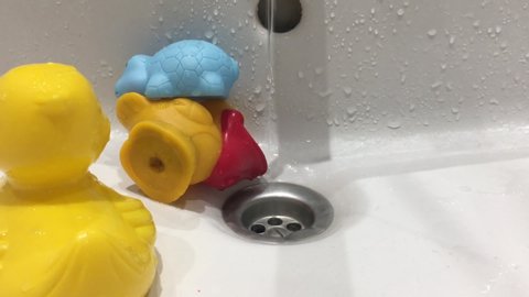 Colourful rubber squishy toys placed under running tap water in sink. Close up. 