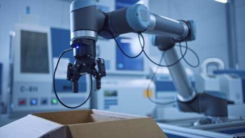 Industry 4.0 Modern Factory: Programmed robot arm Packing Metal Components into Cardboard Box. Production Line Machine Picks and Packs Product into Package. Fully Automated Warehouse Robotics