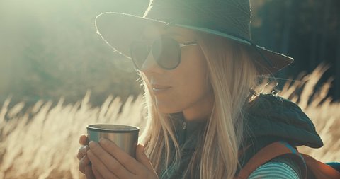 Close-up Woman hiking backpacker traveler drinking hot tea and relaxing in the fall forest on sunny autumn day. Beautiful mountain landscape view. 4K slow motion video.
 วิดีโอสต็อก
