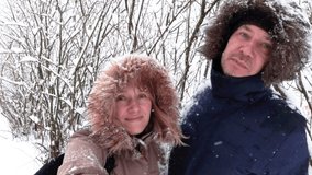Middle aged man and woman laugh smile and shake bush with snow. Beautiful winter season landscape. Trees under white snow. New Year and Christmas concept. Nature walk in park. Stock video