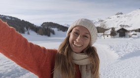 Woman traveling in Switzerland in winter taking selfie video portrait in the mountains having fun in winter wonderland. One woman video chat on phone 