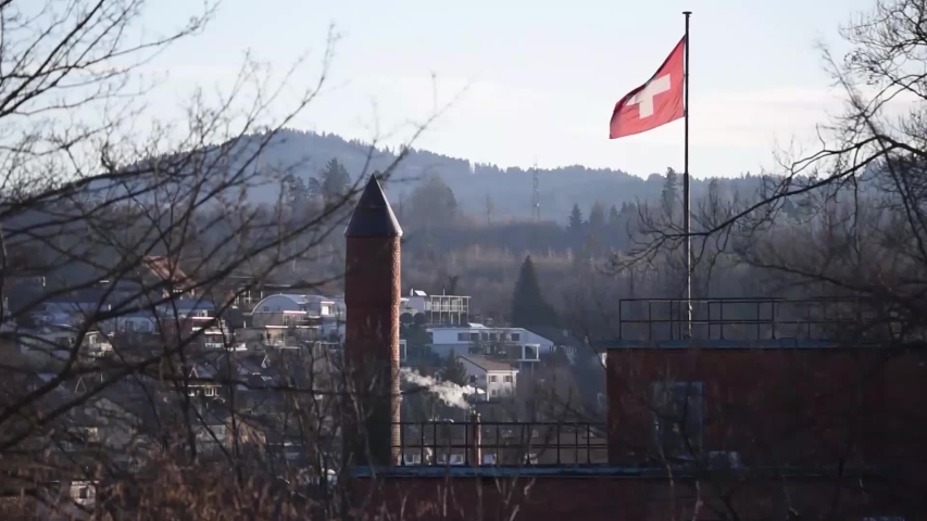 A Swiss flag waving with the wind in Uster. Farm animals and nature noice background.  Early winter time.