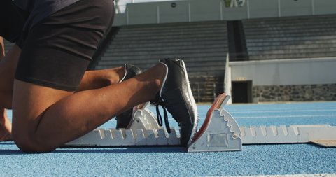 Side view close up of a mixed race male athlete practicing at a sports stadium, starting sprinting from running blocks, slow motion