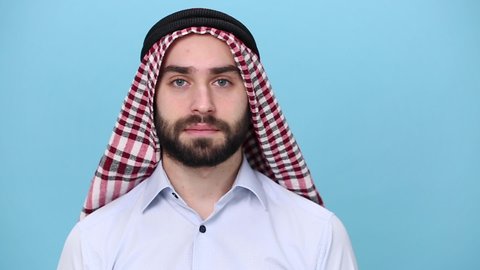 Bearded young arabian muslim man 20s in keffiyeh kafiya ring igal agal casual clothes posing isolated on pastel blue background. People religious lifestyle concept. Looking at camera, fooling around