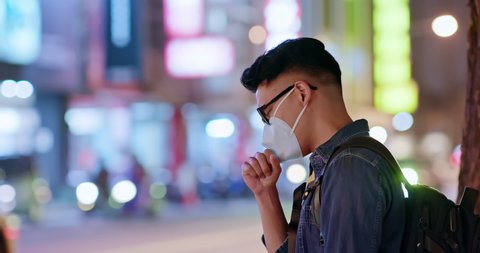 Asian man coughs and wears protective mask because of transmissible infectious diseases or air pollution in the city at night