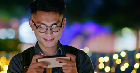 asian young man win mobile games on smart phone with fist gesture outdoor in the evening