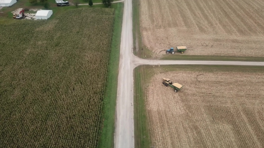 Aerial view of a gravel road in rural Iowa; on one side of the road is harvested corn field and on the other side of the road is a farmstead and a corn field that is not yet ready for harvest