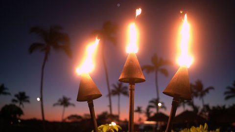Hawaii sunset with fire torches. Hawaiian icon, lights burning at dusk at beach resort or restaurants for outdoor lighting and decoration, cozy atmosphere.

