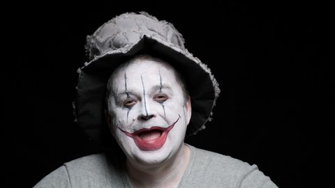 Portrait of a clown man in a hat grimaces on a black background.