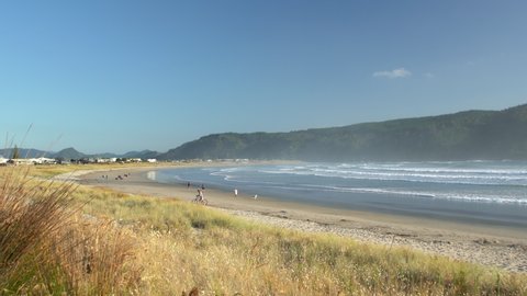 Whangamata, Waikato, / New Zealand - January 21 2020: Local people and holidaymakers walking along a beach at sunrise as waves break in the background.